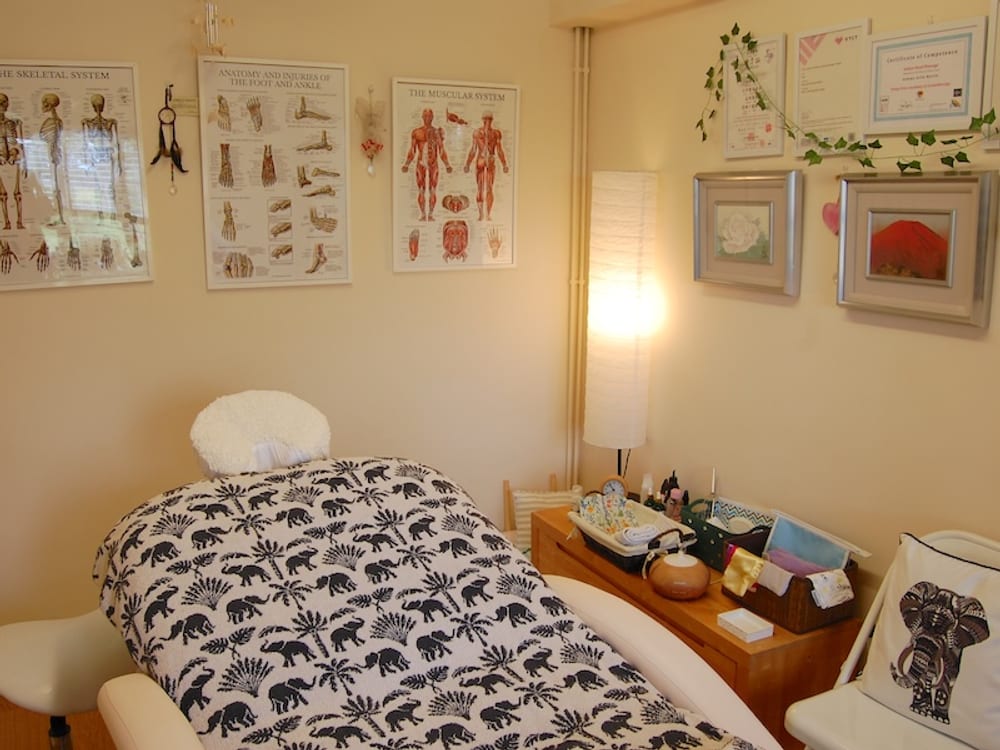 Gemma's treatment room – the massage couch with a patterned throw, anatomy charts on the wall, and a softly lit lamp
