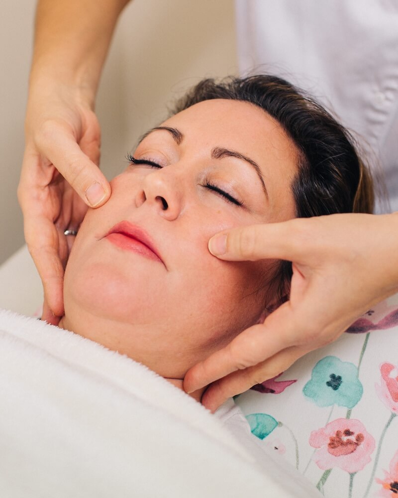 Gemma performing facial reflexology on a client, applying gentle pressure with her fingertips
