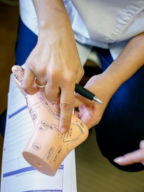 Gemma using a reflexology foot chart model to explain the reflex points to a client