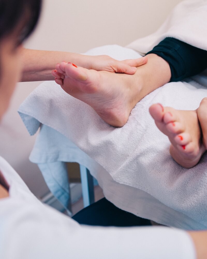 Close-up of reflexology lymph drainage being performed on a client's feet, raised on a white treatment bolster